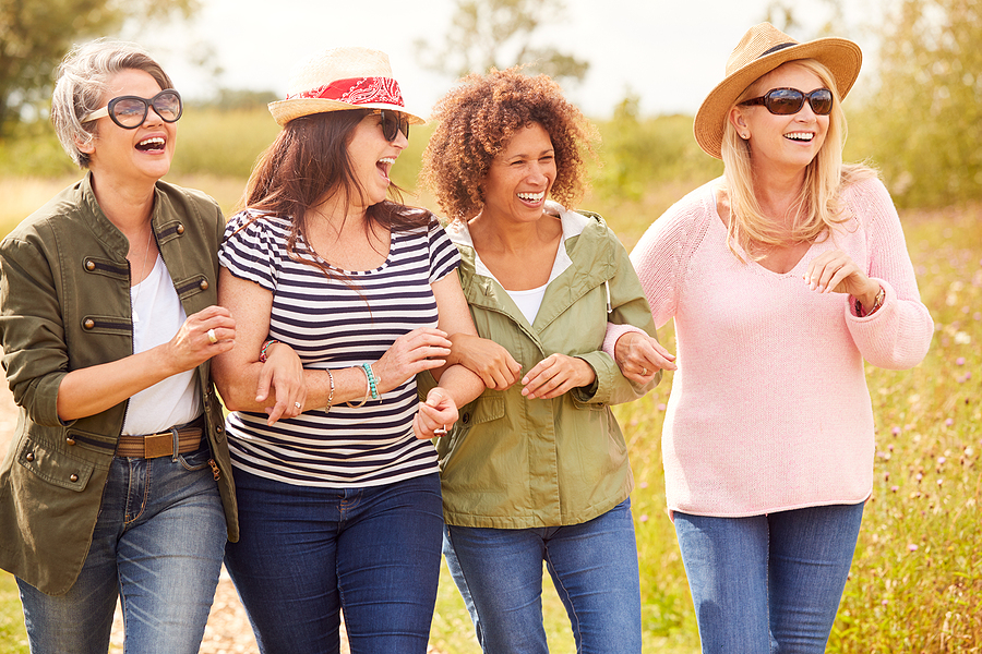 Mature female friends walking together arm in arm and laughing outdoors on a sunny day.