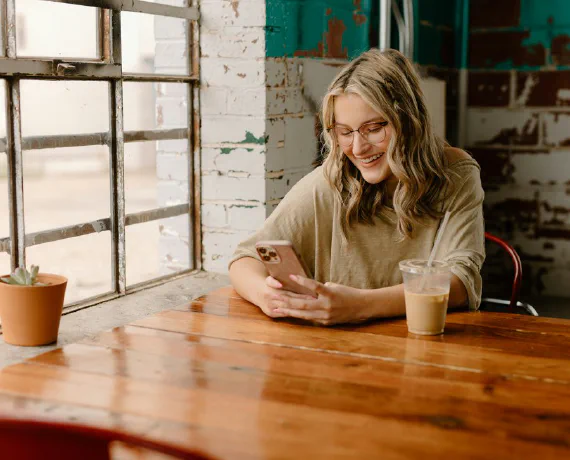 A woman smiling at her phone in a cafe